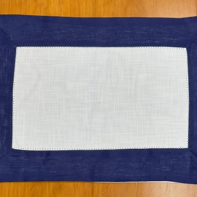 Individual retangular branco com borda azul escura sobre mesa de madeira