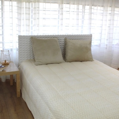 Cama de casal com cabeceira estofada branca e almofadas cinza junto a janela com cortinas brancas