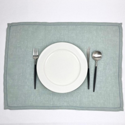 Conjunto de pratos branco com talheres de cabo preto sobre individual azul esverdeado