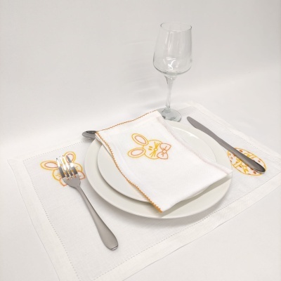 Conjunto de mesa com prato branco, talheres metálicos, copo transparente e toalhete bordado com coelho amarelo