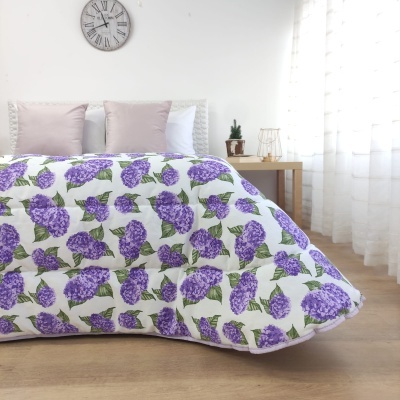 Cobertor florido lilás e verde em cama com almofadas e mesa ao lado