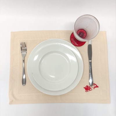 Lugar de mesa com prato branco, talheres metálicos, copo transparente com base vermelha sobre base de tecido bege