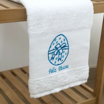 Toalha branca com bordado azul de ovo de páscoa e texto 'Feliz Páscoa'