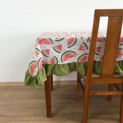 toalha de mesa branca com estampado de melancia e borda verde numa mesa de madeira com cadeira