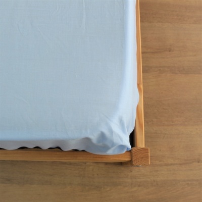 Canto de cama de madeira clara com lençol azul claro sobre chão em madeira.