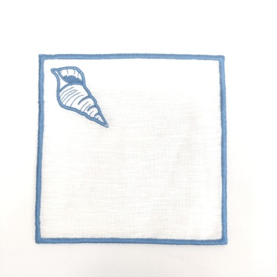 Guardanapo branco com borda azul e concha azul no canto superior esquerdo