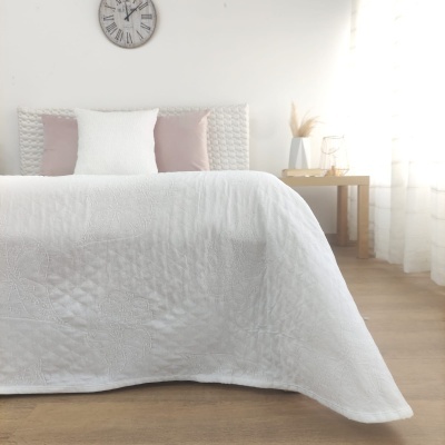 Cama com edredão branco e almofadas, relógio de parede e mesa de madeira com jarro e vaso decorativo