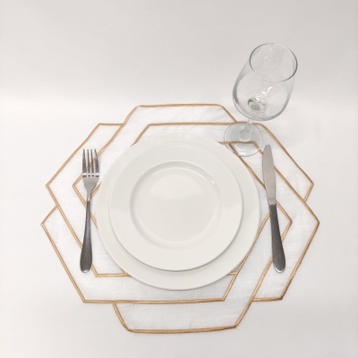 Conjunto de loiça branca com talheres e taça em cima de placemats hexagonais brancos com bordas douradas