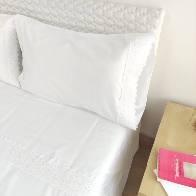 Conjunto de roupa de cama branca com bordados geométricos e mesa de cabeceira ao lado
