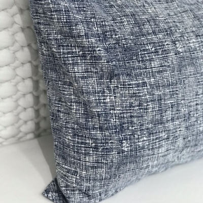 Travesseiro decorativo cinza e azul com padrão texturizado sobre superfície branca