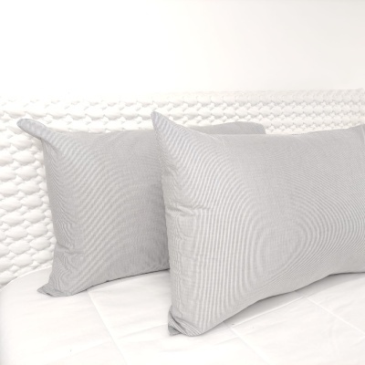 Dois almofadões cinzentos sobre cama branca com cabeceira texturada em malha grossa branca