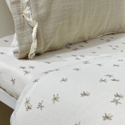 Lençol branco com estrelas castanhas e almofada bege texturizada com franjas