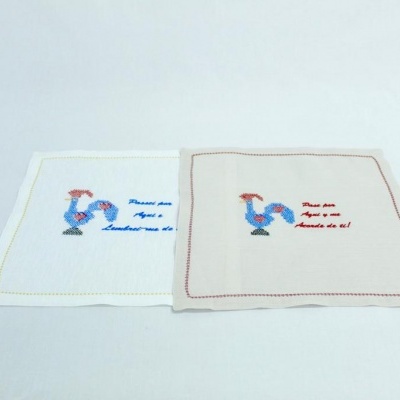 Dois panos de cozinha bordados, um branco e outro bege, com galo e texto