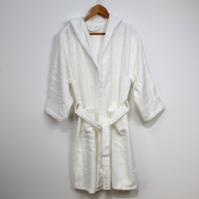 Roupão branco felpudo com capuz pendurado num cabide de madeira