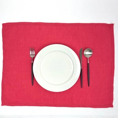 Conjunto de lugar de mesa com individual vermelho, pratos brancos e talheres com cabos pretos