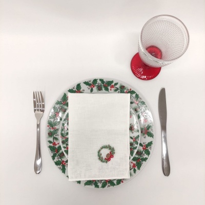 Mesa posta com prato decorado com azevinho, guardanapo branco, talheres e copo com base vermelha