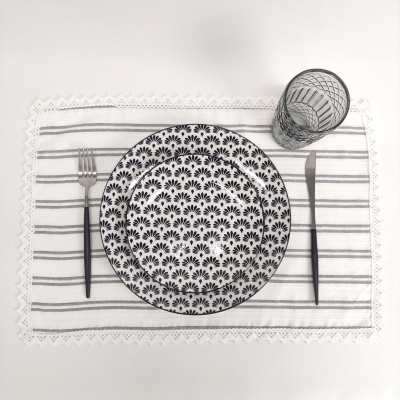 Conjunto de loiça com padrões pretos, talheres pretos e copo de vidro sobre toalhete branco com riscas.