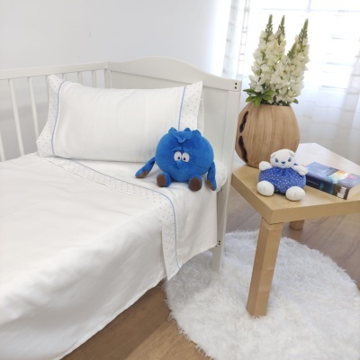 Cama infantil com roupa de cama branca e peluches coloridos ao lado numa mesa de madeira clara