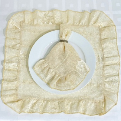 Guarda-napo dourado com padrão floral subtil num prato branco sobre pano de mesa branco quadriculado