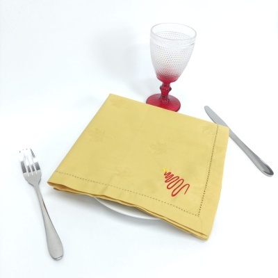 Guardanapo amarelo com bordado vermelho sobre prato branco, talheres e copo com base vermelha