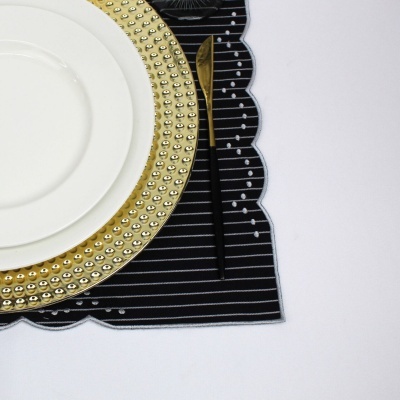 Conjunto de pratos branco e dourado com faca dourada sobre suporte preto listrado e superfície branca
