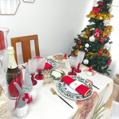 Mesa de jantar decorada para Natal com pratos, copos, guardanapos, figuras de rena e gnomos, e árvore de Natal ao fundo