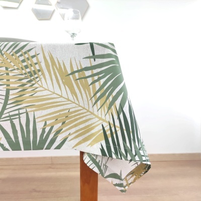 Toalha de mesa branca com padrão de folhas tropicais verdes e beges em mesa de madeira.