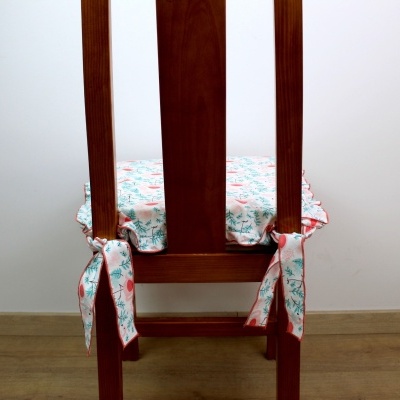 Cadeira de madeira escura com almofada floral amarrada ao encosto.