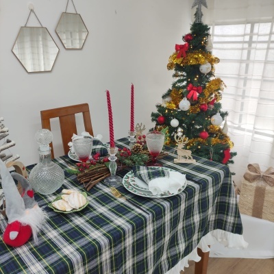 Mesa de jantar decorada com toalha xadrez e decoração natalícia junto a árvore de Natal decorada