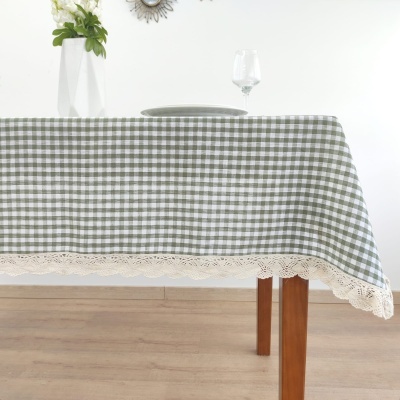 Toalha de mesa xadrez verde e branco com borda rendada creme sobre mesa de madeira
