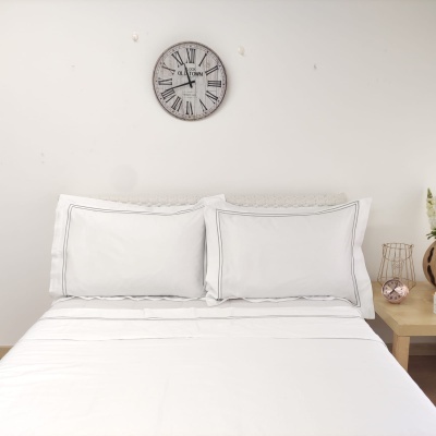 Cama arrumada com roupa branca e relógio de parede com números romanos.