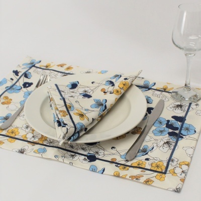 Jogo americano e guardanapo de tecido com padrão floral azul e amarelo, prato branco e talheres