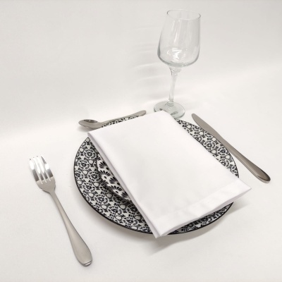 Conjunto de jantar com prato preto e branco, guardanapo branco, talheres metálicos e copo de vidro