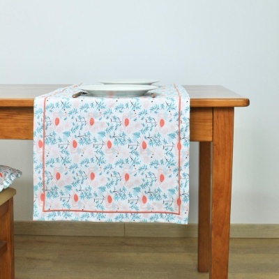 Caminho de mesa branco com padrão de folhas verdes e frutos laranja sobre mesa de madeira.