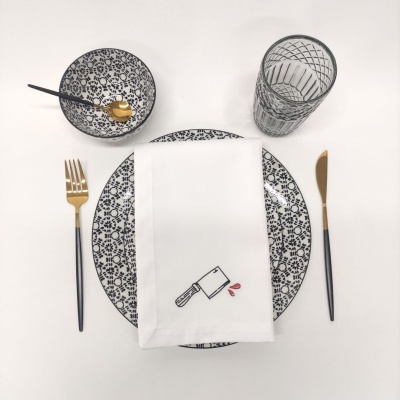 Conjunto de loiça preto e branco com talheres e guardanapo branco com desenho de cutelo.