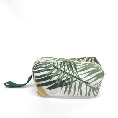 Necessaire em tecido com padrão de folhas verdes e amarelas, fecho de correr e alça lateral verde