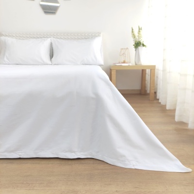 Cama com roupa de cama branca, mesa de cabeceira com vaso e cortina translúcida