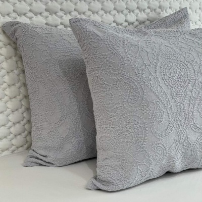 Almofadas cinzentas com padrão texturizado detalhado sobre cama com colcha branca