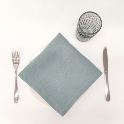 Conjunto de mesa com prato branco, guardanapo cinza, talheres de metal e copo de vidro