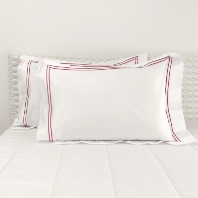 fronhas brancas com bordado vermelho em cama com edredão branco e cabeceira almofadada