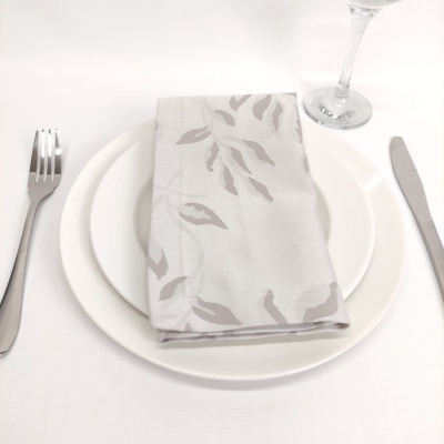 Conjunto de jantar com pratos brancos, guardanapo cinzento claro com padrão de folhas e talheres prateados