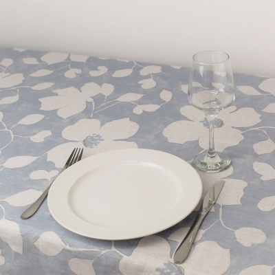 Mesa posta com toalha azul claro com flores brancas, prato branco, talheres e copo