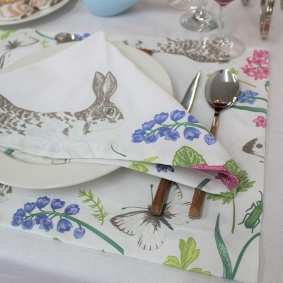 Jogo americano e guardanapo com padrão de coelho e flores coloridas, talheres e prato numa mesa posta