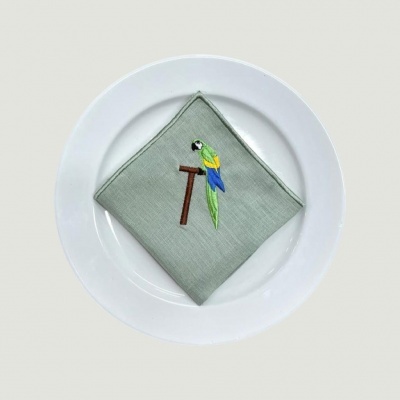 Guardanapo cinza claro com bordado de papagaio colorido no prato branco