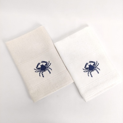 Duas toalhas, creme e branca, com bordado azul de caranguejo