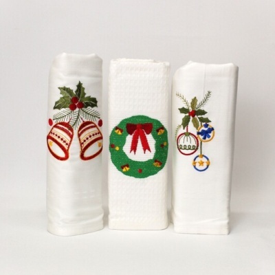 Três panos de cozinha brancos com bordados natalícios de sinos, guirlanda e bolas de Natal.