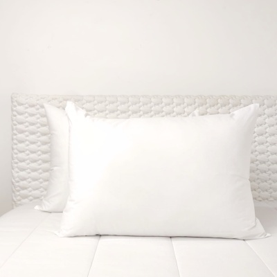 Três almofadas brancas numa cama com cabeceira acolchoada cinzenta