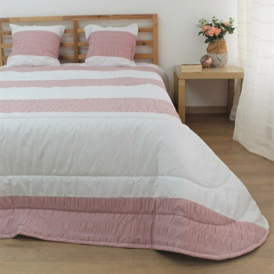 Colcha branca com riscas cor-de-rosa e almofadas correspondentes numa cama de madeira clara