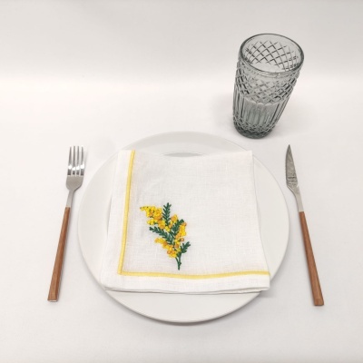 Conjunto de mesa com prato branco, guardanapo bordado, talheres com cabo castanho e copo de vidro texturizado