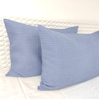 Duas almofadas azuis com padrão quadrado em cama com cabeceira branca acolchoada